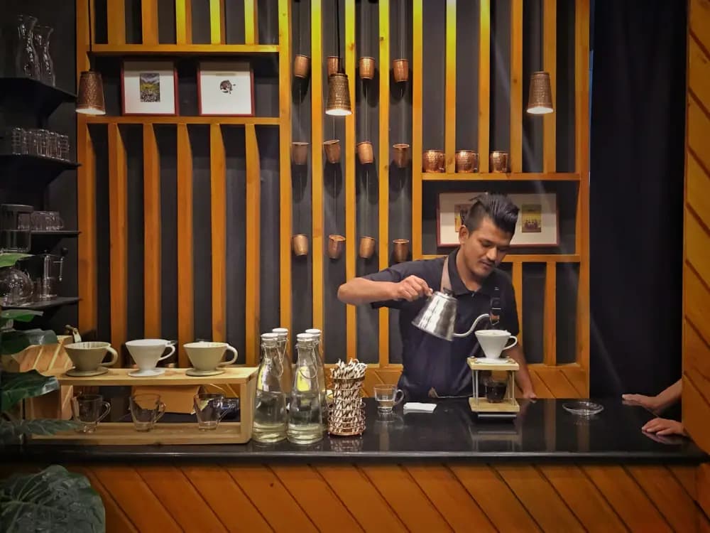 A barista pouring coffee behind the wooden counter of a café in Kathmandu